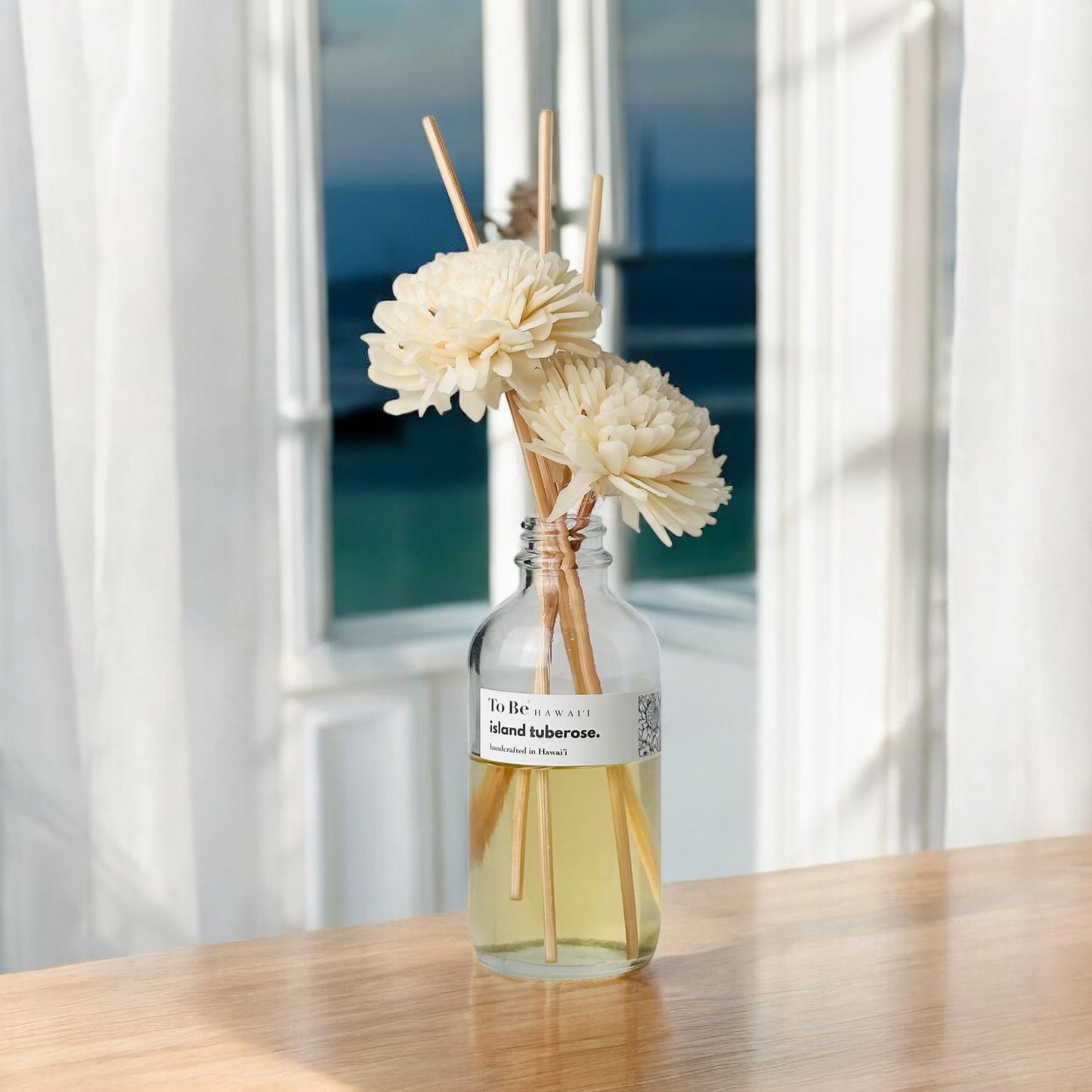 Diffuser with flowers on a wooden table in front of a window