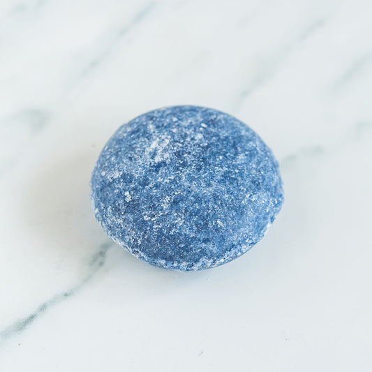 A blue shampoo bar for men centered on a white marble surface