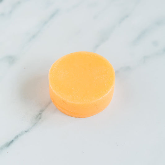 An orange, round best bar conditioner centered on a marble surface.
