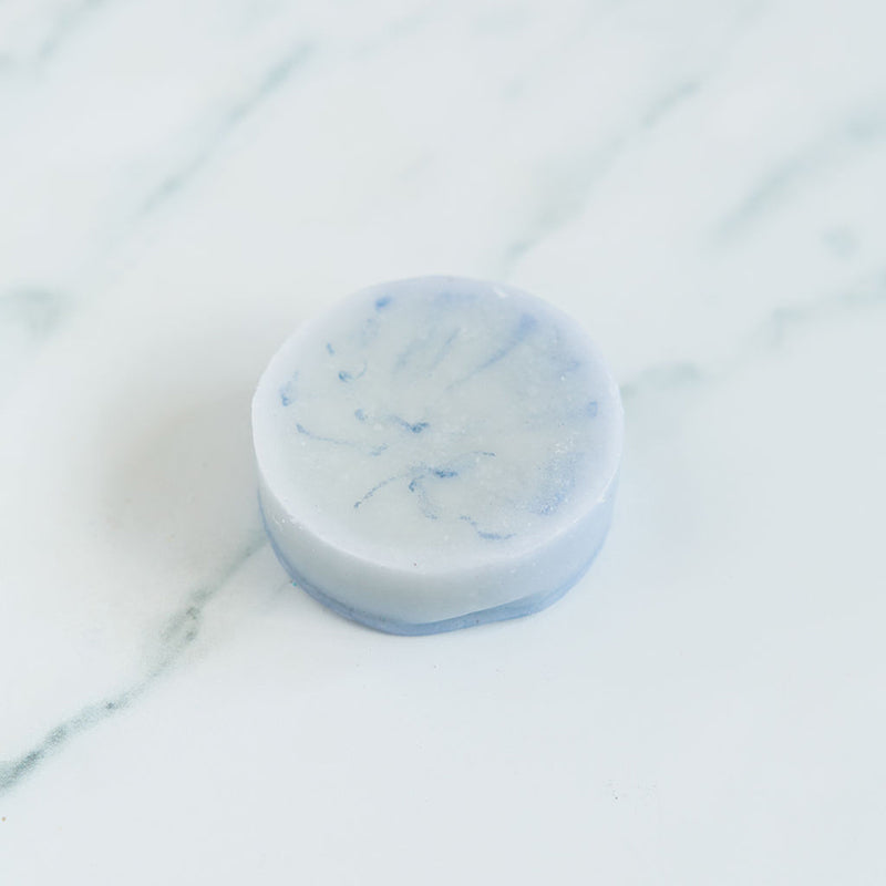 A blue conditioner bar soap for men centered on a marble surface