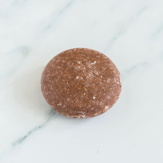 A round natural shampoo bar placed on a marble surface