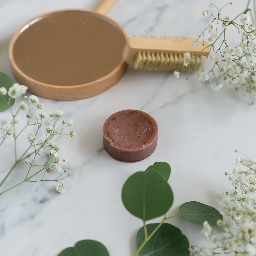 Conditioner bar on a marble background next to brush and flower