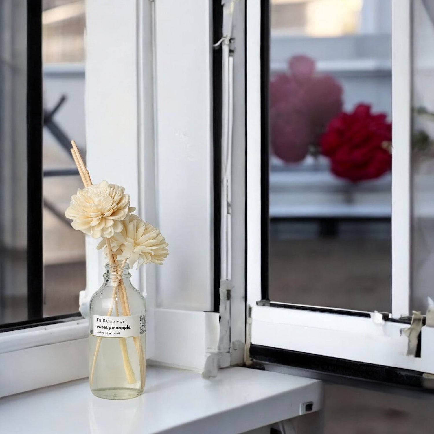 Sweet Pineapple Reed Diffuser by revivEARTH with a wood flower reed in a glass bottle, sitting on a bright white windowsill.