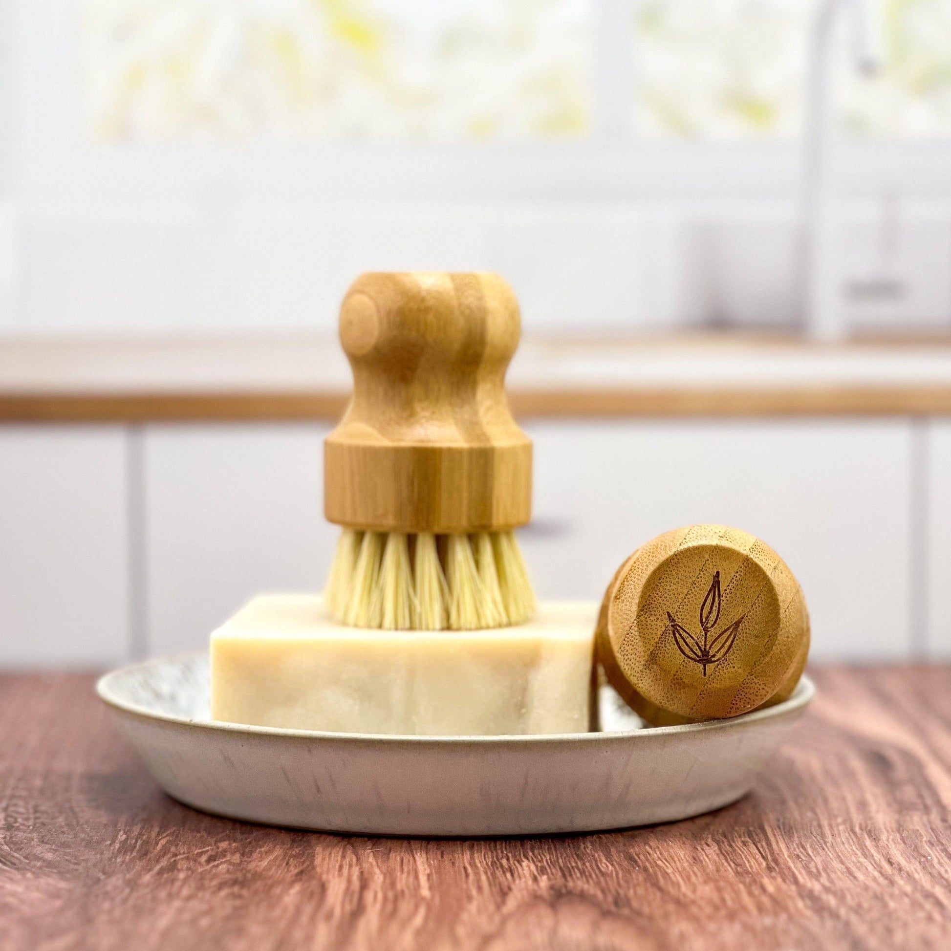 Bamboo pot brush with wooden handle and scrubber, soap bar, and lid on a wooden surface.