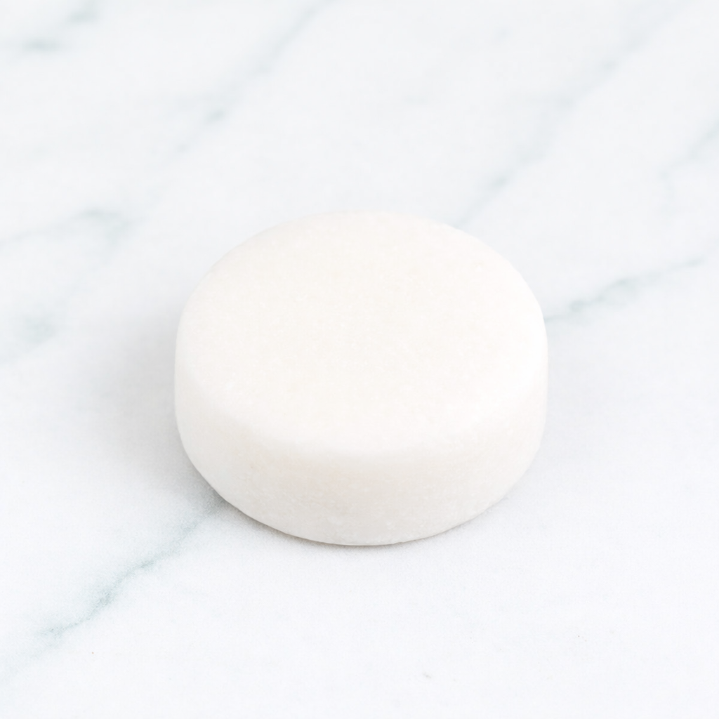 A clean, aesthetic shot of a smooth Citrus Mint Conditioner Bar centered on marble. The image features orange slices and fresh mint leaves, showcasing the zero-waste, plastic-free packaging and its refreshing, shine-enhancing formula.