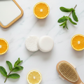 A vibrant top-down shot of the Citrus Mint Shampoo and Conditioner bars side-by-side on a white marble background. The duo is surrounded by a bright arrangement of fresh orange slices, lemon halves, and green mint leaves, emphasizing a refreshing hair care set.