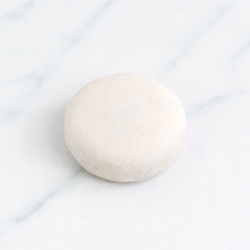 A round Citrus Mint Shampoo Bar on a white marble surface eco-friendly wooden bath accessories.