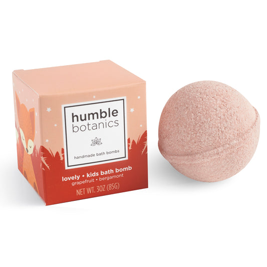 A single pink KIDS Lovely Bath Bomb next to its orange and white "Humble Botanics" packaging, designed as a gentle bath bomb for kids.