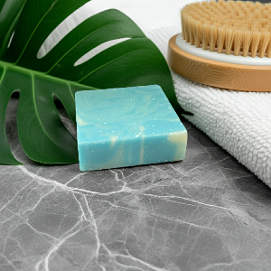 Blue soap bar on a marble surface with a green leaf and wooden brush in the background