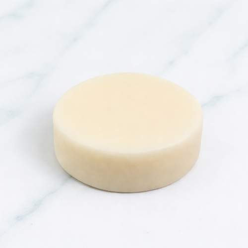 A high-resolution product shot of a round, off-white Rosemary Conditioner Bar with the name embossed on top. The bar is perfectly centered on a white marble background.