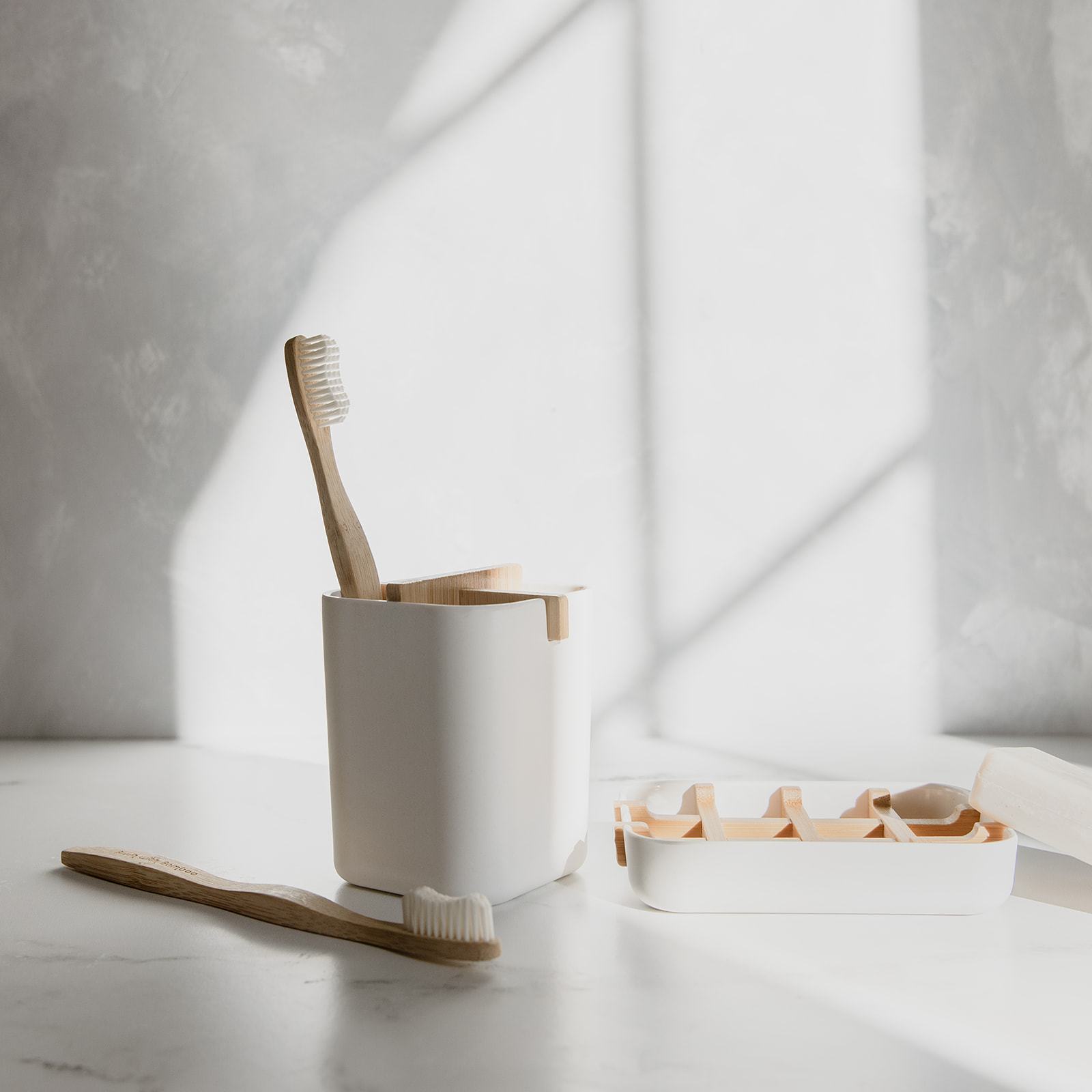 Bamboo toothbrushes in a white cup on a light surface with a neutral background