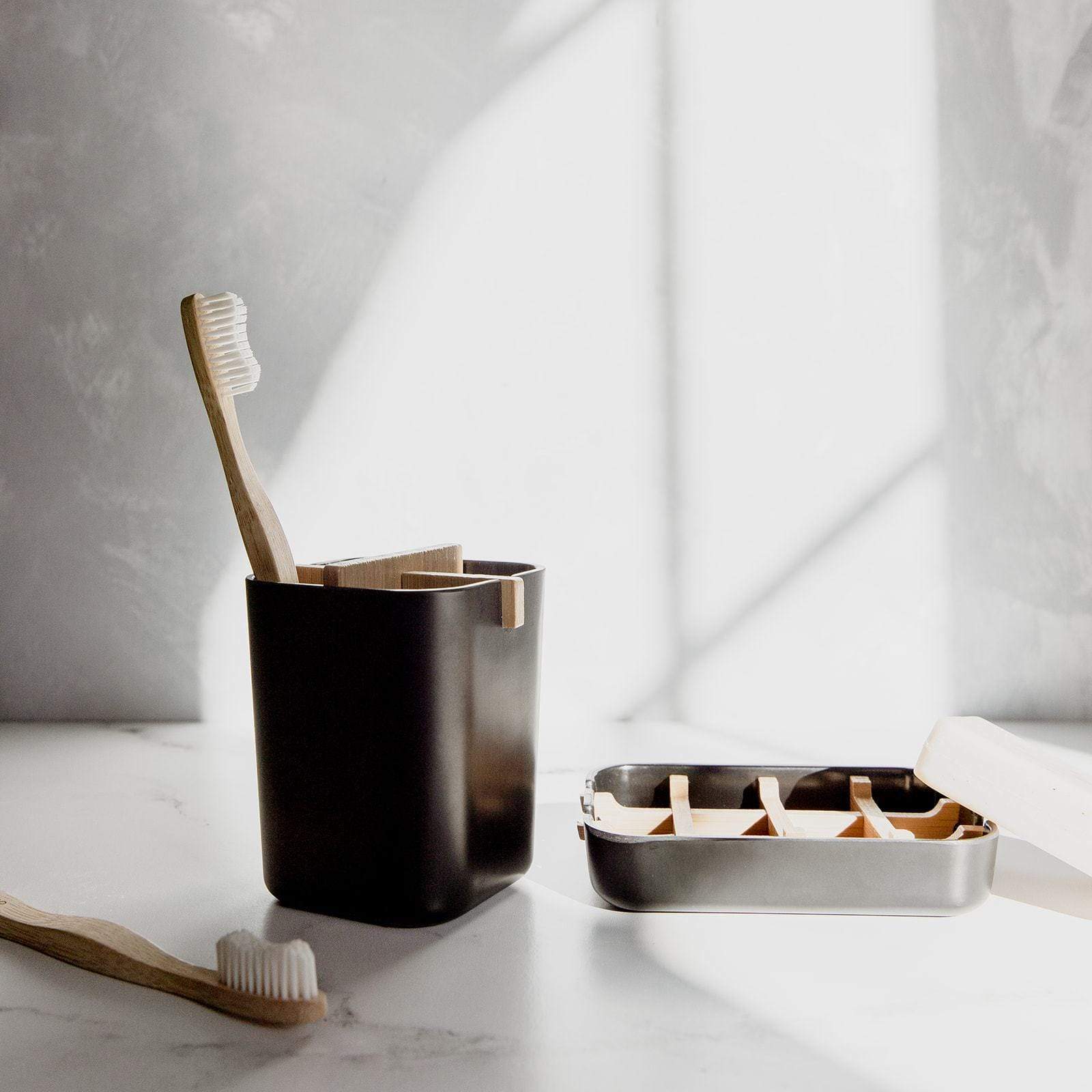 Black toothbrush holder with wooden toothbrushes on a marble surface.