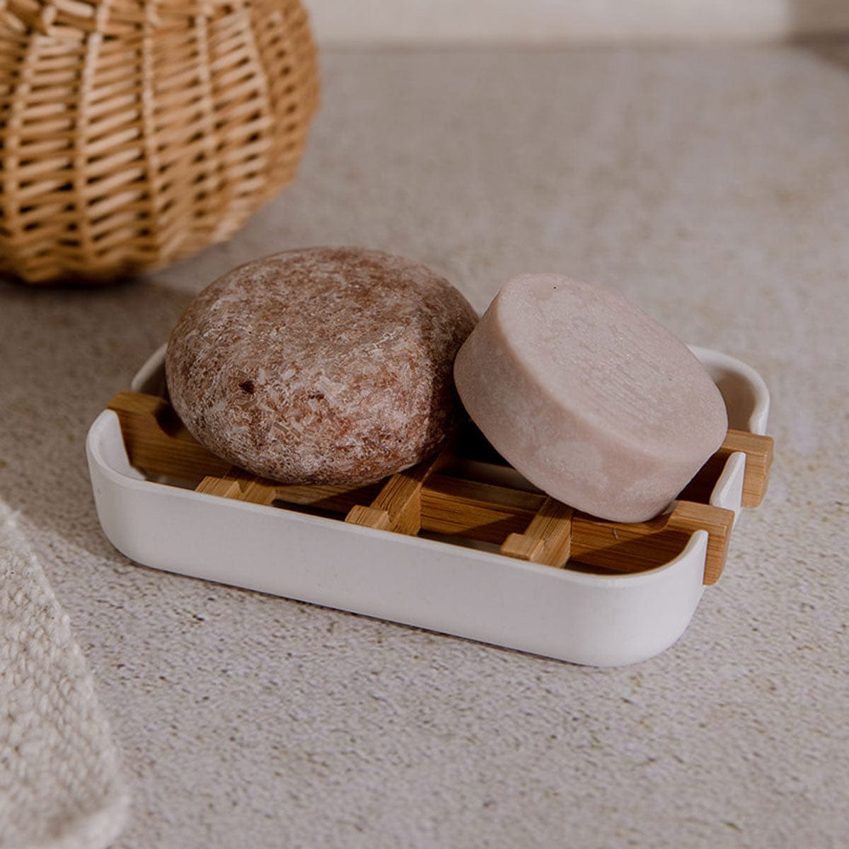 Shampoo and conditioner bars on a white soap dish next to a woven basket.