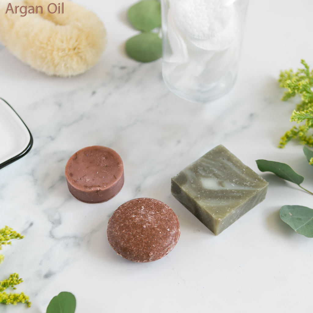 An assortment of solid shampoo, conditioner, and soap bars in various colors displayed on a marble surface.