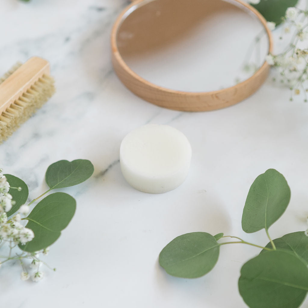 Conditioner bar on a marble counter top next to leaves and  a brush.