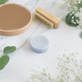 A blue conditioner bar soap for men centered on a marble surface with a wooden nail brush and fresh eucalyptus leaves.