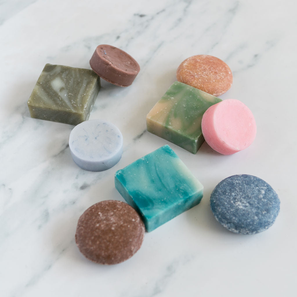 A colorful spa set gift featuring an assortment of round and square revivEARTH shampoo, conditioner, and soap bars arranged on a white marble surface.