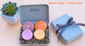 A colorful spa set gift featuring four solid shampoo and conditioner bars in pink, orange, purple, and yellow, presented in an eco-friendly molded pulp box with a decorative ribbon.