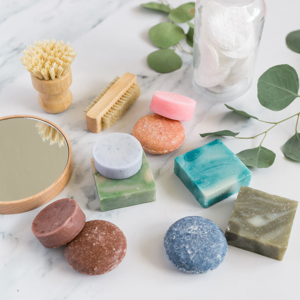 bar shampoos and conditioners next to a wooden mirror, brushes, soap and leaves.